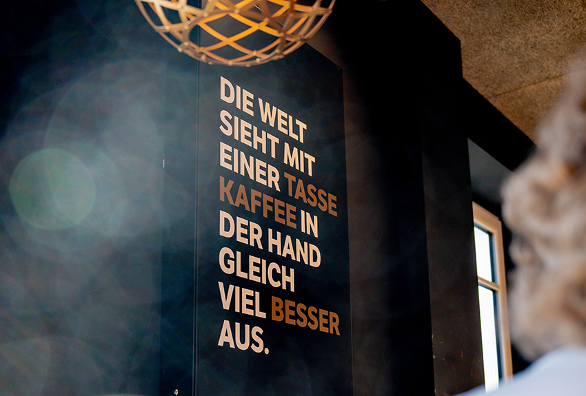 Schild einer modernen Bäckerei mit der Aufschrift Die Welt sieht mit einer Tasse Kaffee in der Hand gleich viel besser aus.